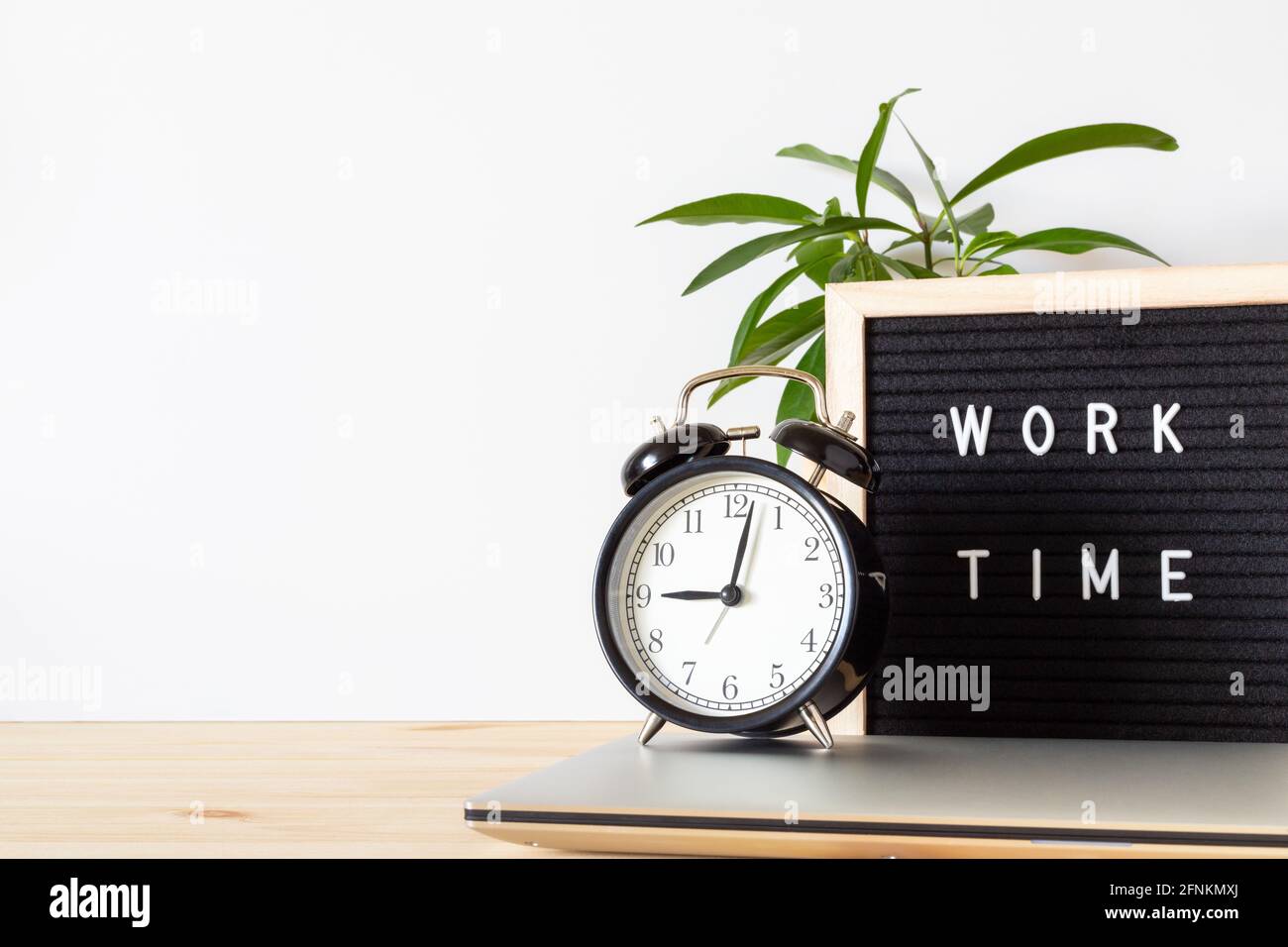 Classic vintage black alarm clock, laptop, potted plant and board sign