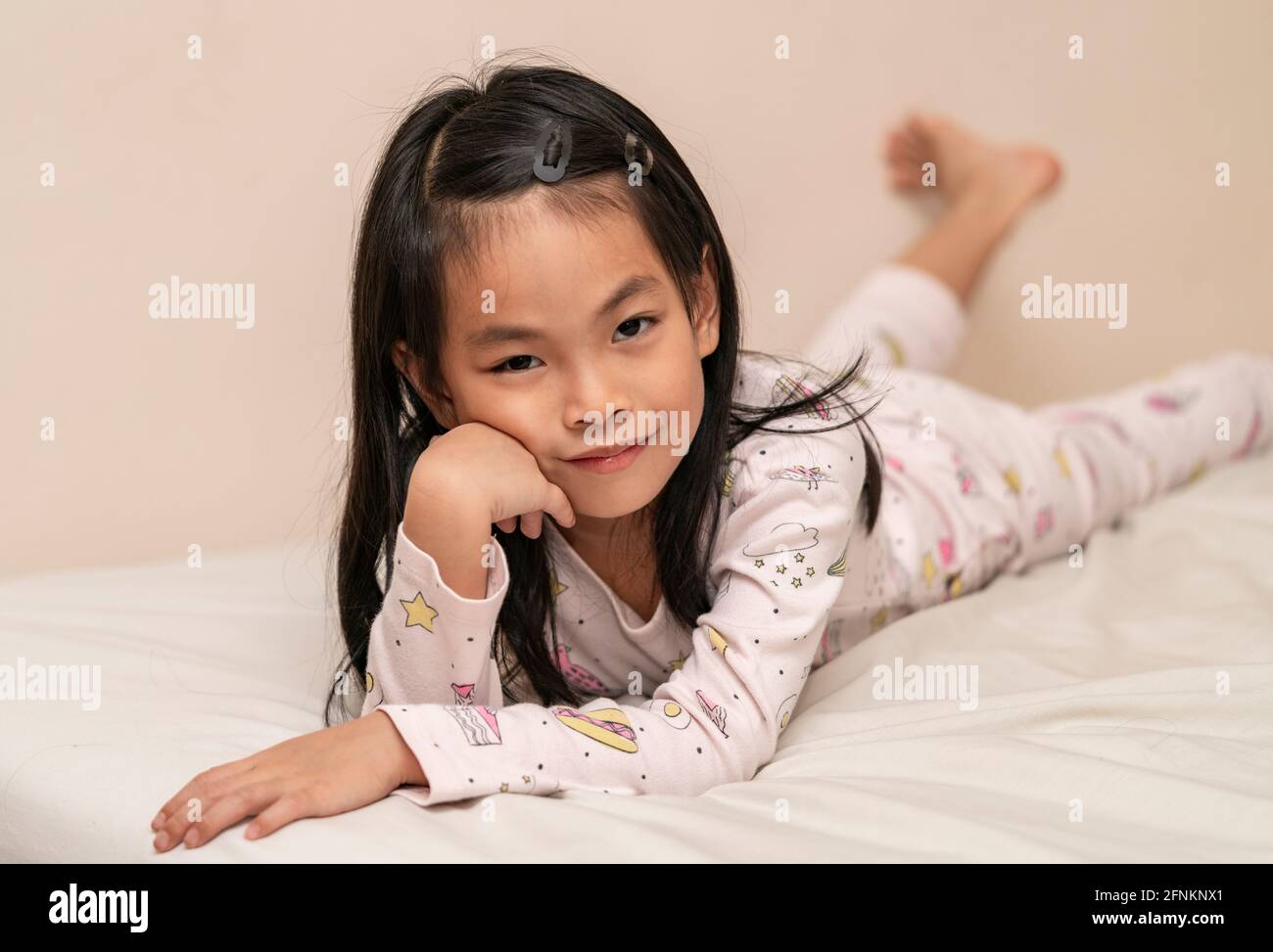 Good looking Asian little girl in pajamas, lying on the bed and leaning