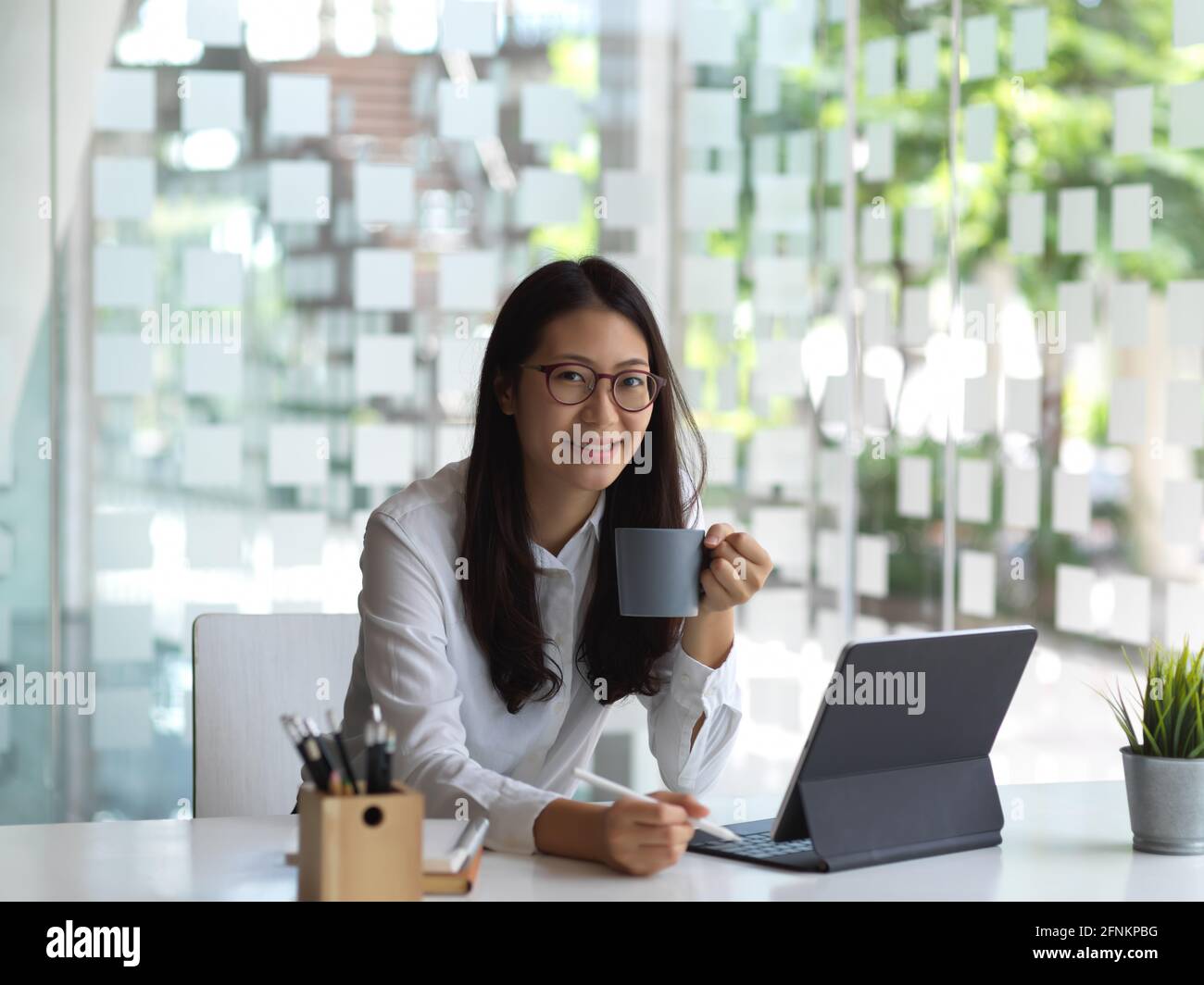 Porttrait of female office worker holding cup while working with tablet and stationery Stock Photo