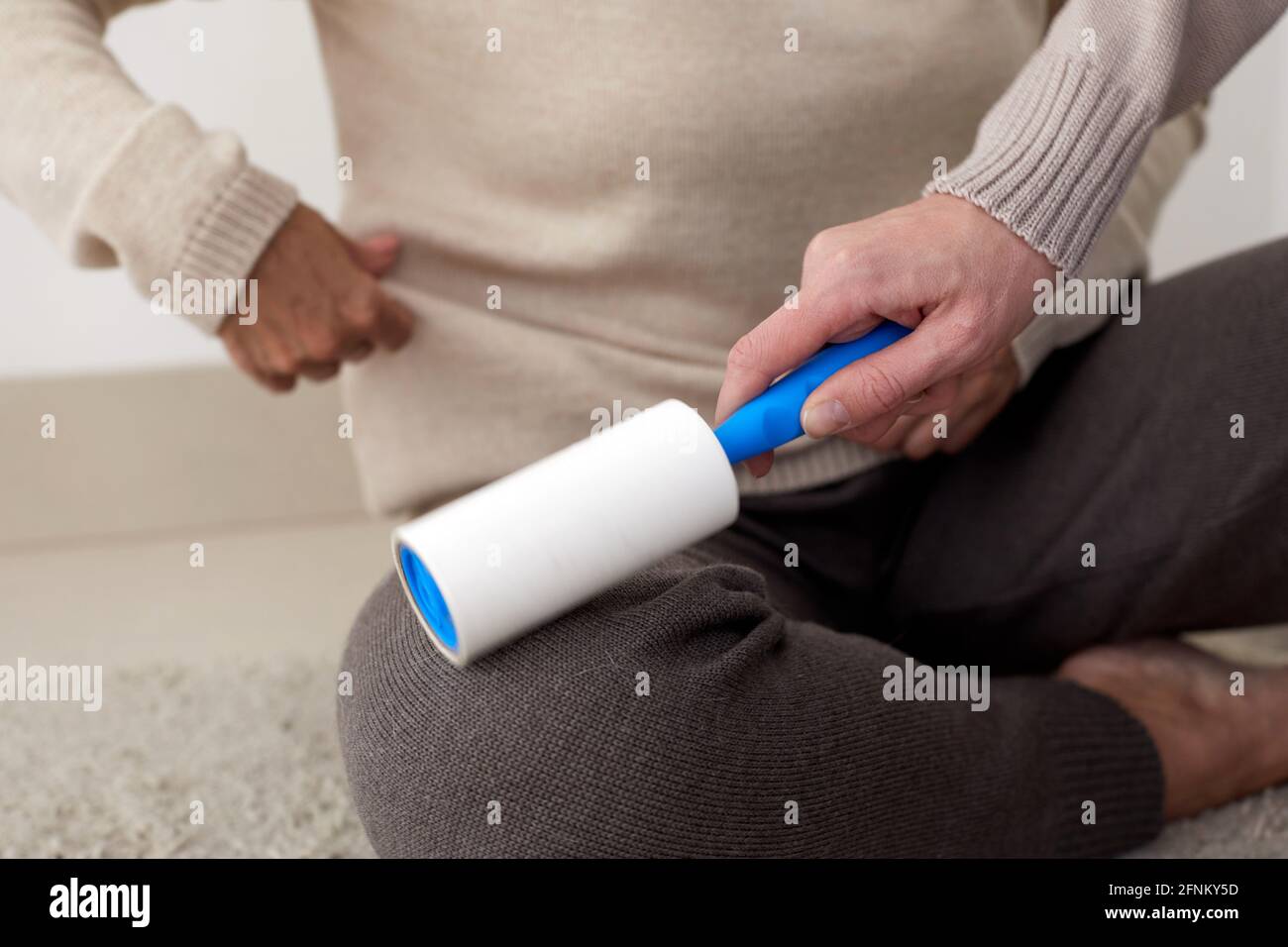 Crop unrecognizable person helping woman and cleaning her clothes with lint roller at home Stock Photo