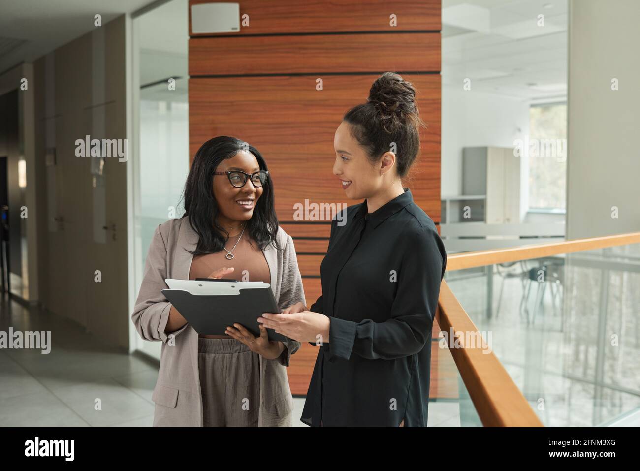Two business colleagues talking to each other and discussing documents while standing in the corridor Stock Photo