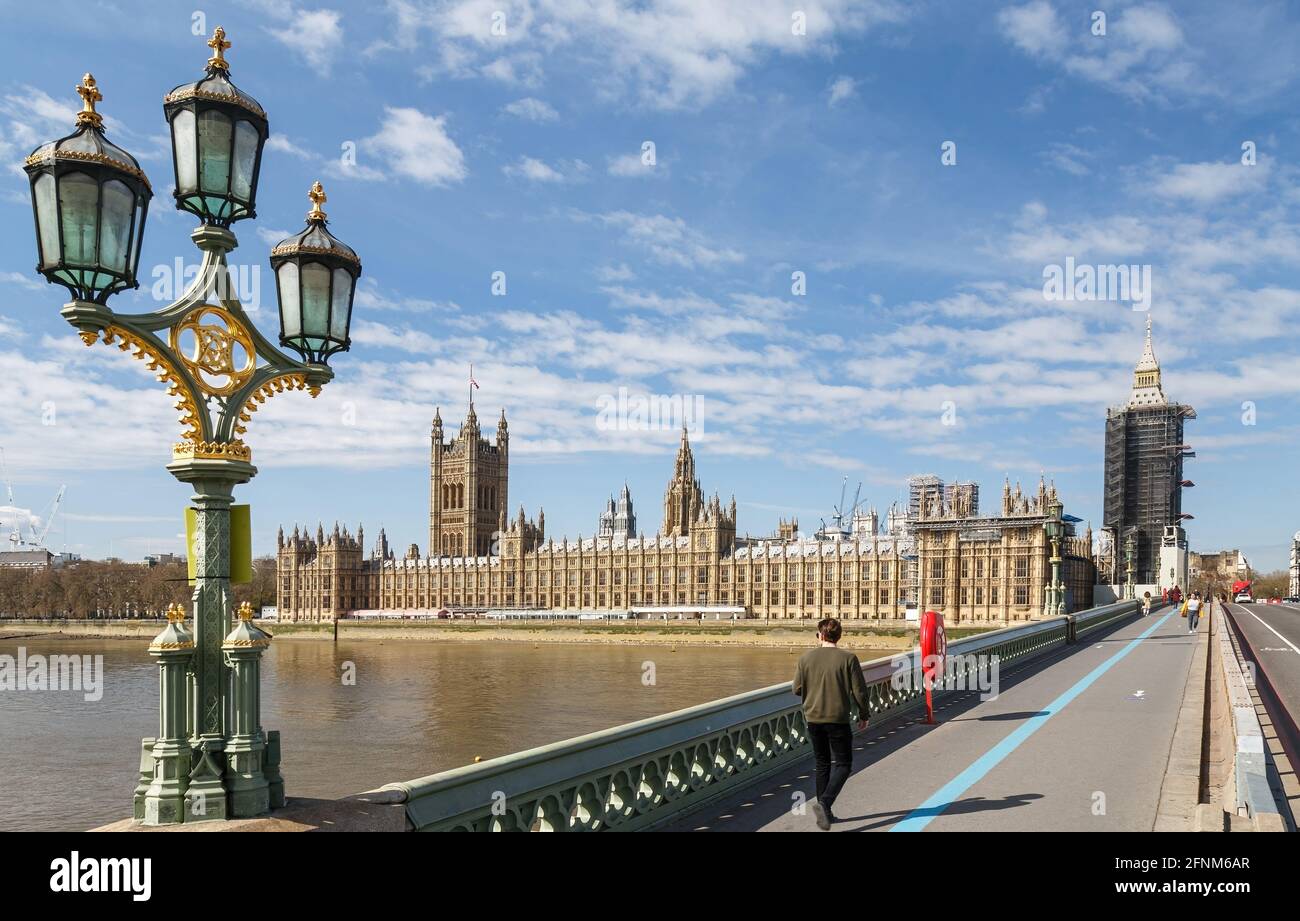 Houses of Parliament from across Westminster Bridge.A few Pedestrians are wearing face masks and traffic is visible at the far end of the bridge. Stock Photo