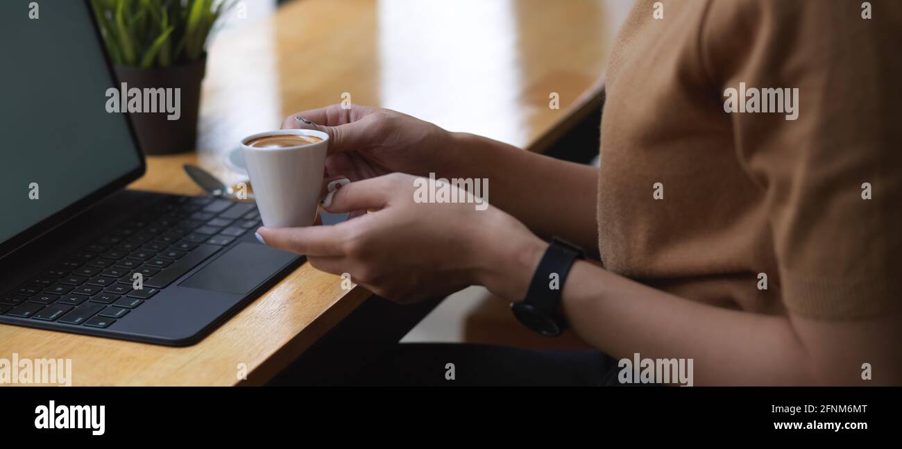 Side view of female hand holding coffee cup while sitting at workplace ...