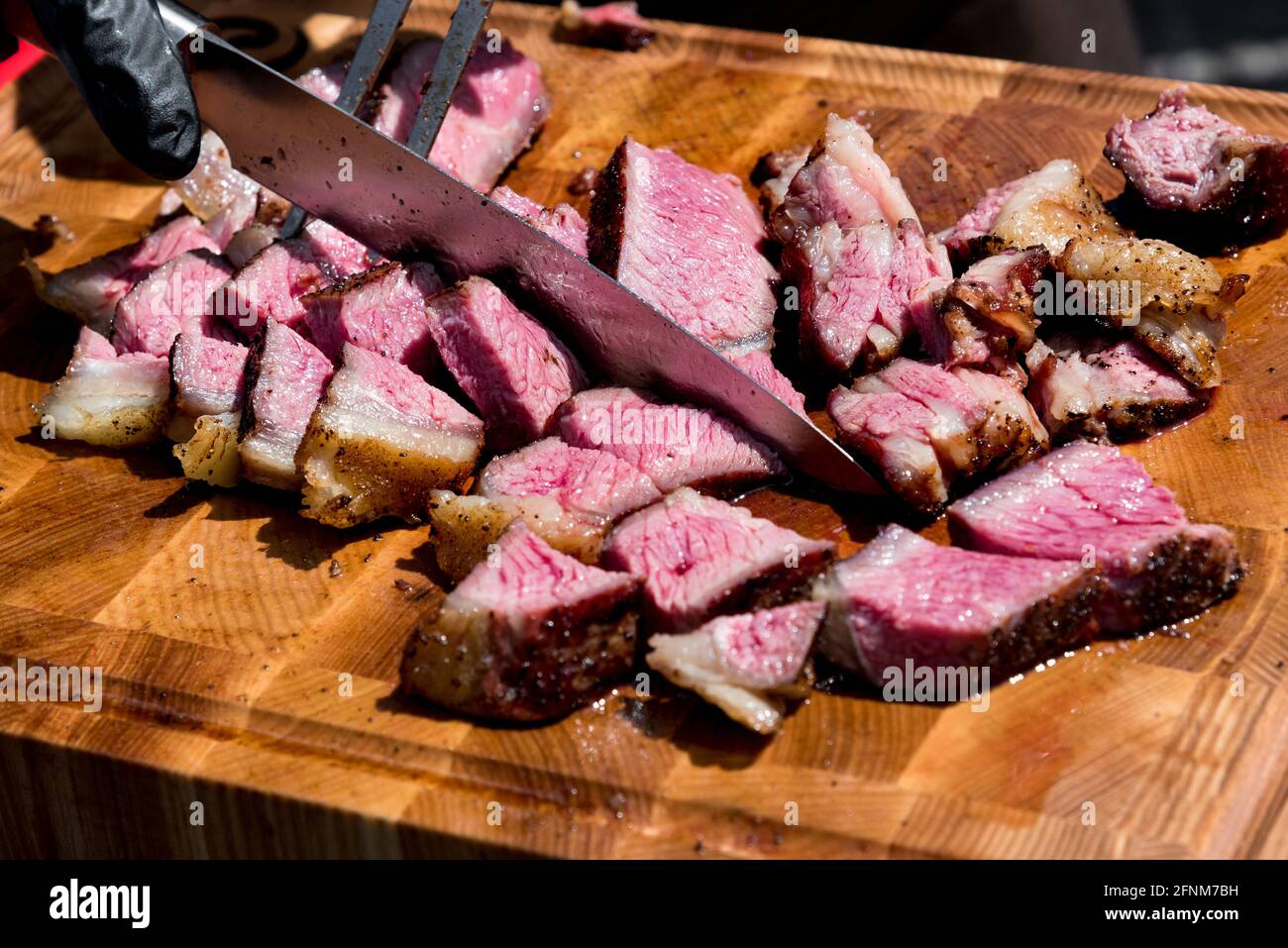 Chef slicing tender medium rare roast beef brisket with a large carving knife in a close up view on the chopping board Stock Photo