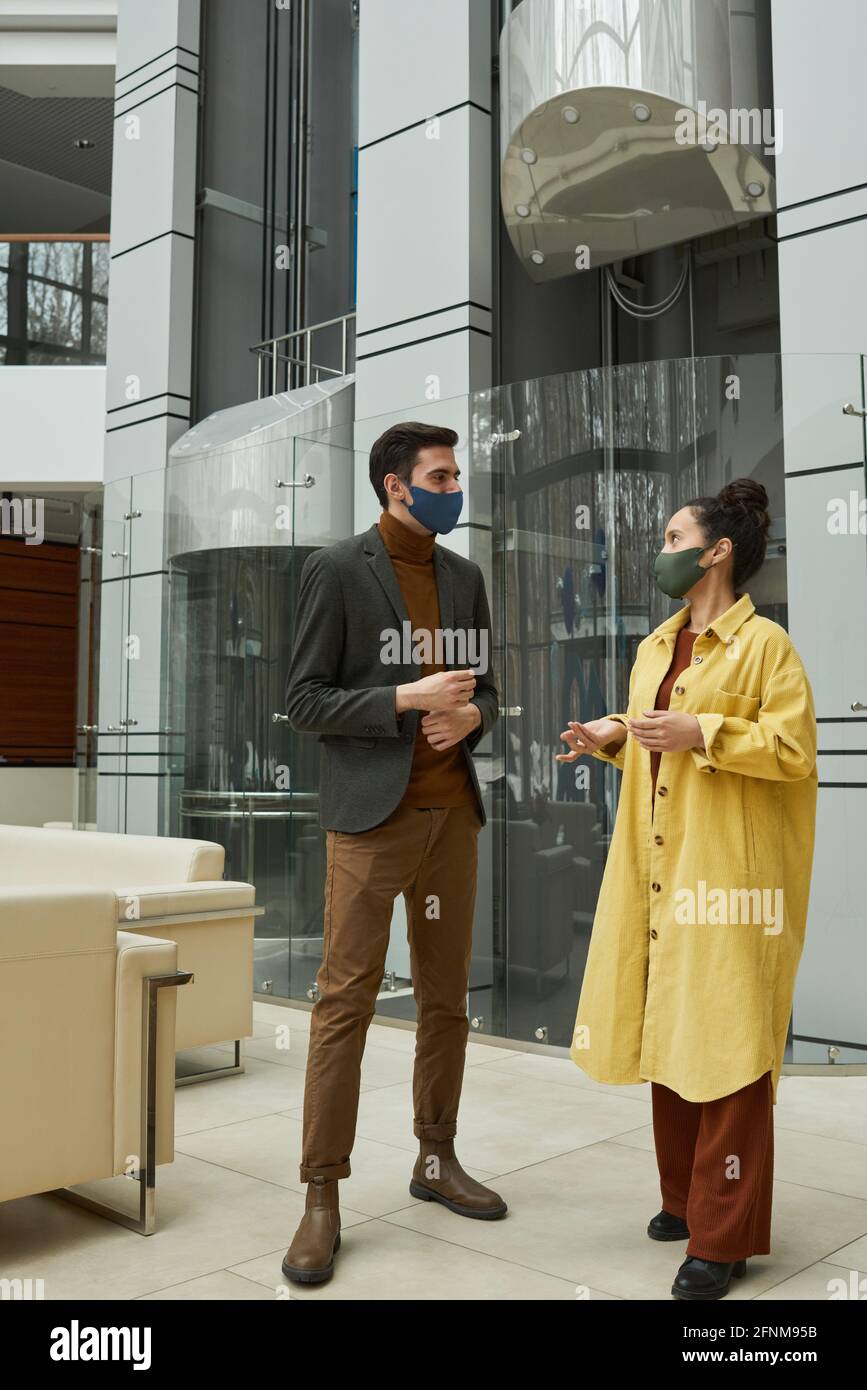 Business colleagues talking in masks while standing at office corridor Stock Photo