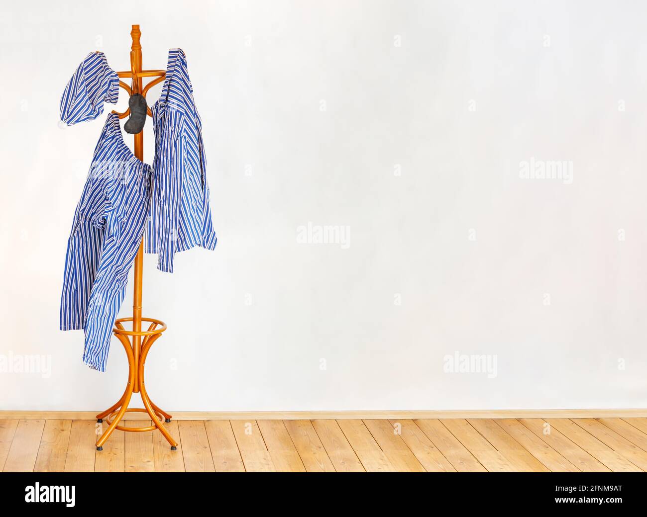 The striped pajamas hangs on the coat hook in an empty room with wooden floor. Stock Photo