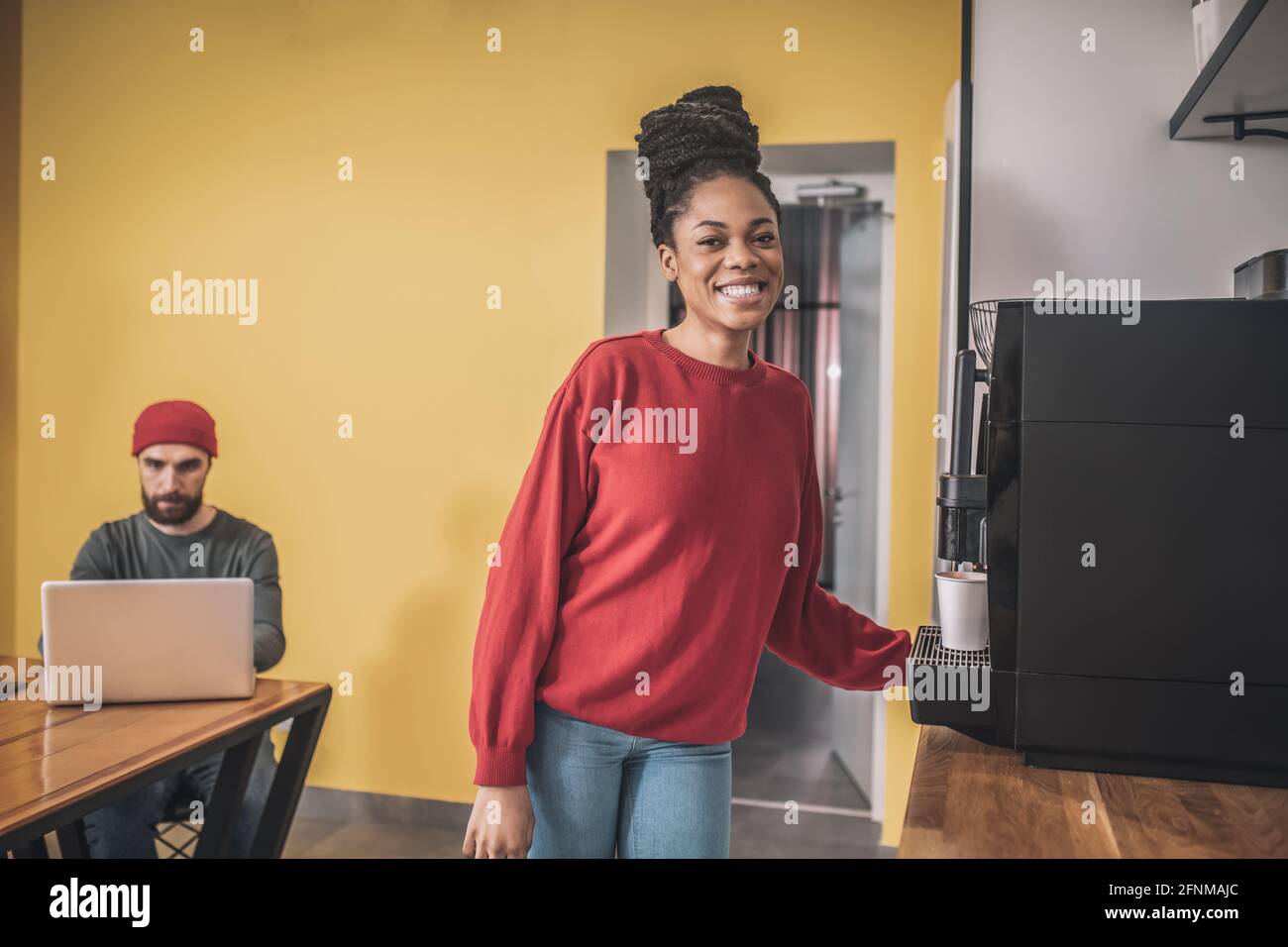 Dark-skinned young woman standing near the coffee-machine Stock Photo