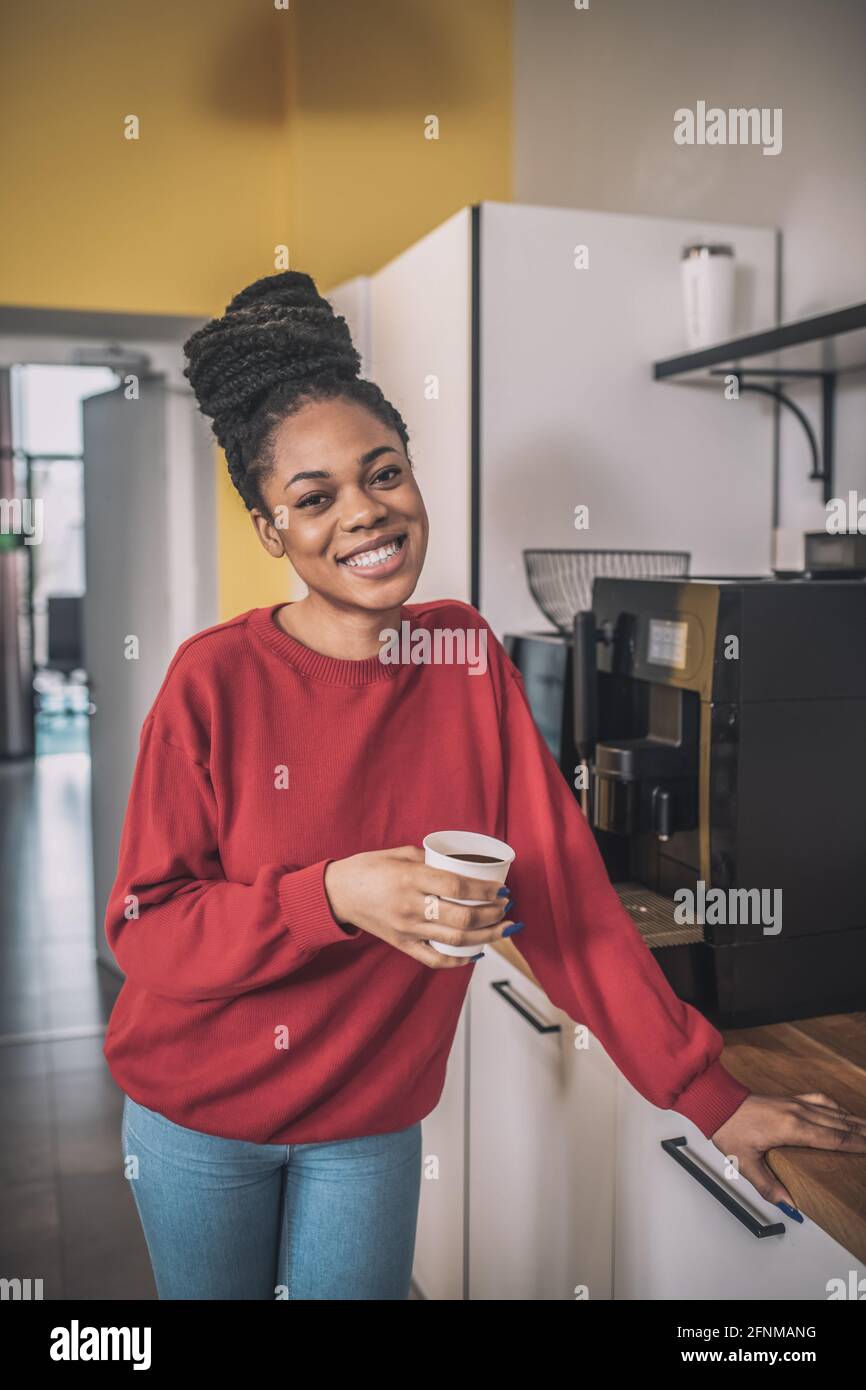 Dark-skinned young woman standing near the coffee-machine Stock Photo