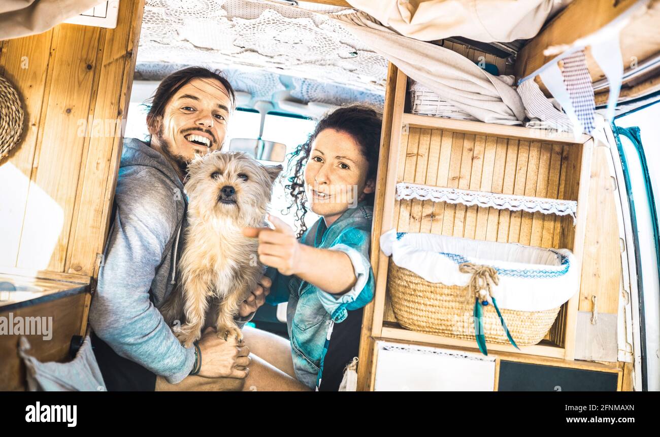 Hipster couple with cute dog traveling together on oldtimer mini van transport - Travel lifetstyle concept with indie people on minivan adventure trip Stock Photo