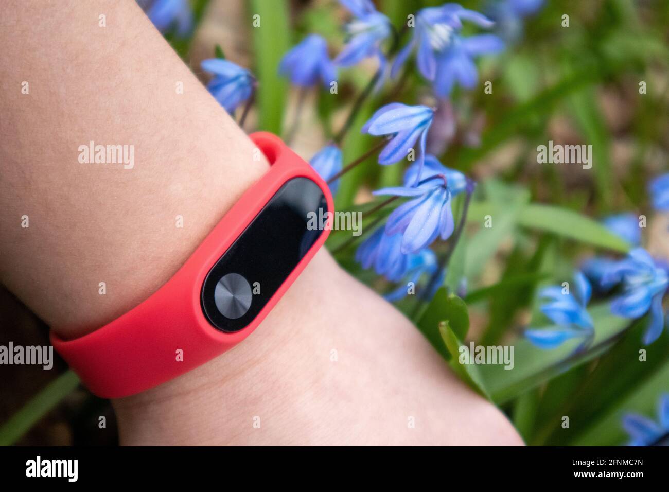 Fitness Tracker With Red Band On Wrist Close Up In Spring Blue Flowers Outdoor Activity