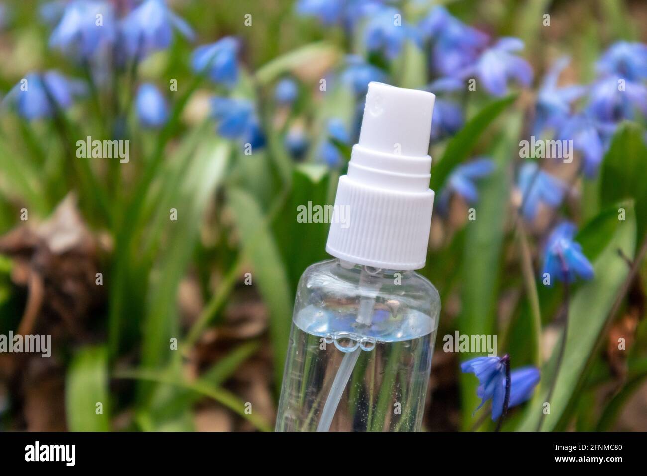 Clear liquid spray pump bottle in blooming pretty flower lawn of blue