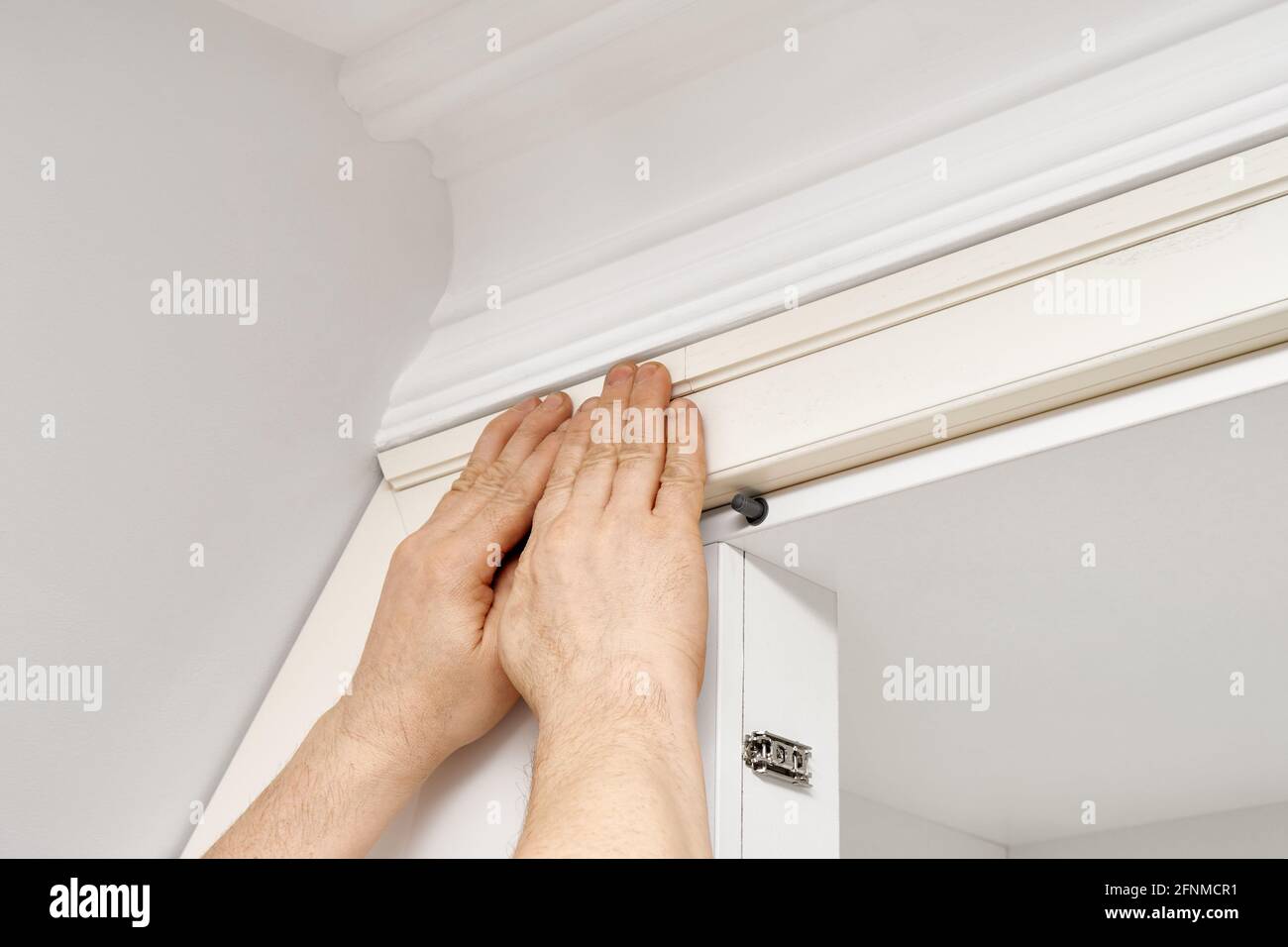 Skilled handyman gluing wooden molding during wardrobe installation in light room extreme close view Stock Photo