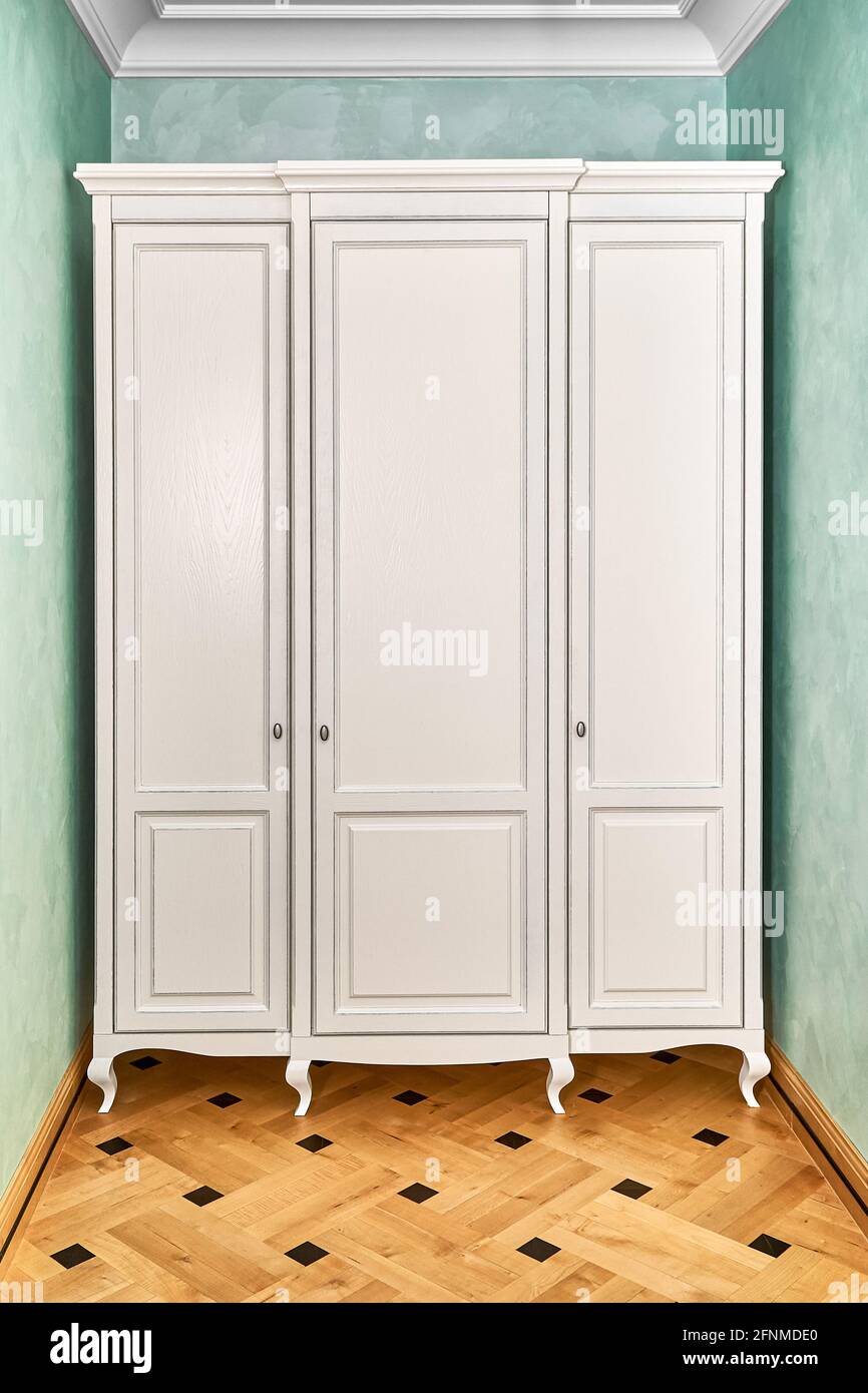Three-section white wardrobe in classic style with carved legs in a modern  hallway with green walls and elegant vintage wooden block parquet floor  Stock Photo - Alamy