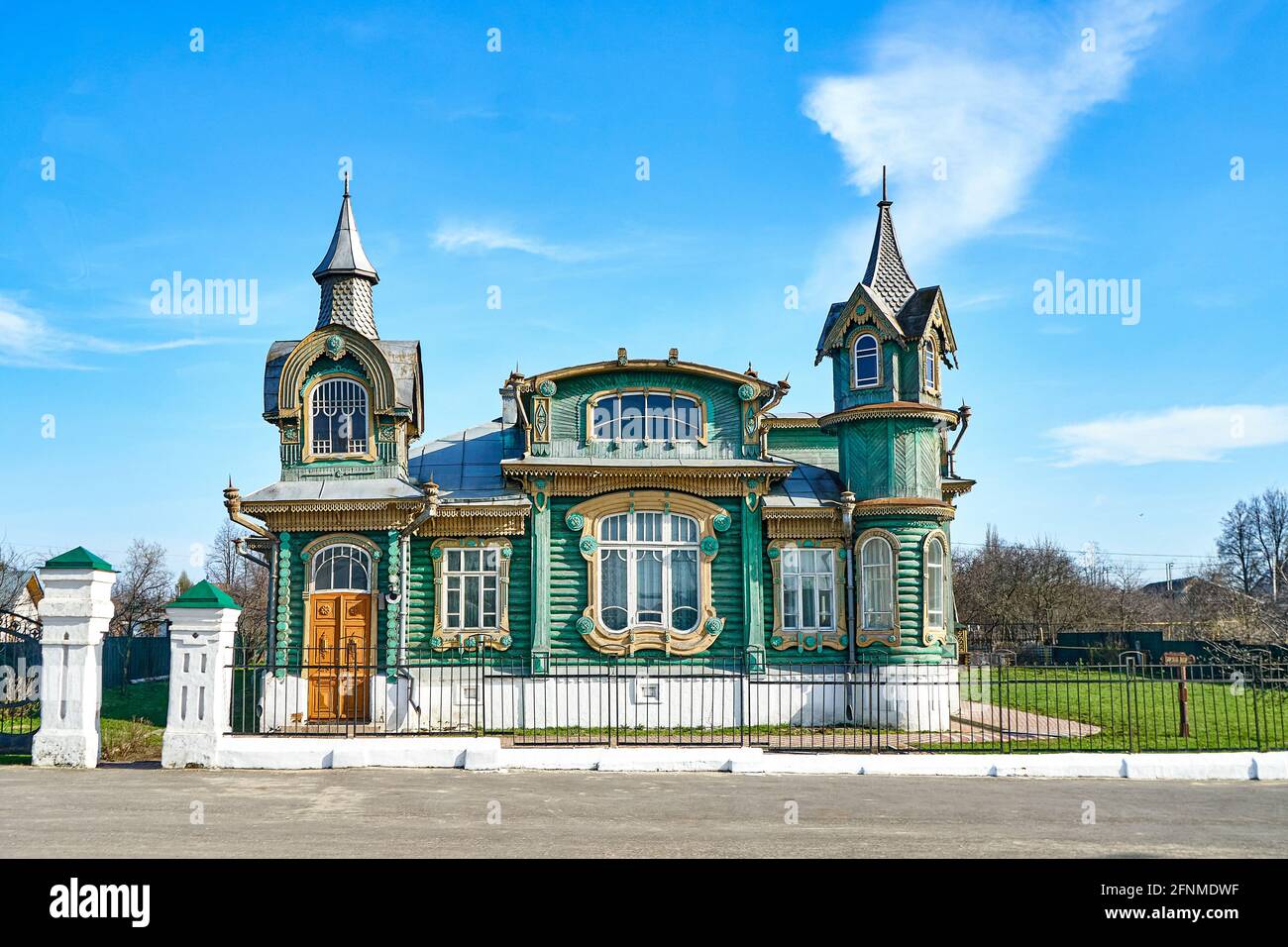 Stylish green vintage log building with spires on towers and decorated windows on village street under blue sky on summer day Stock Photo