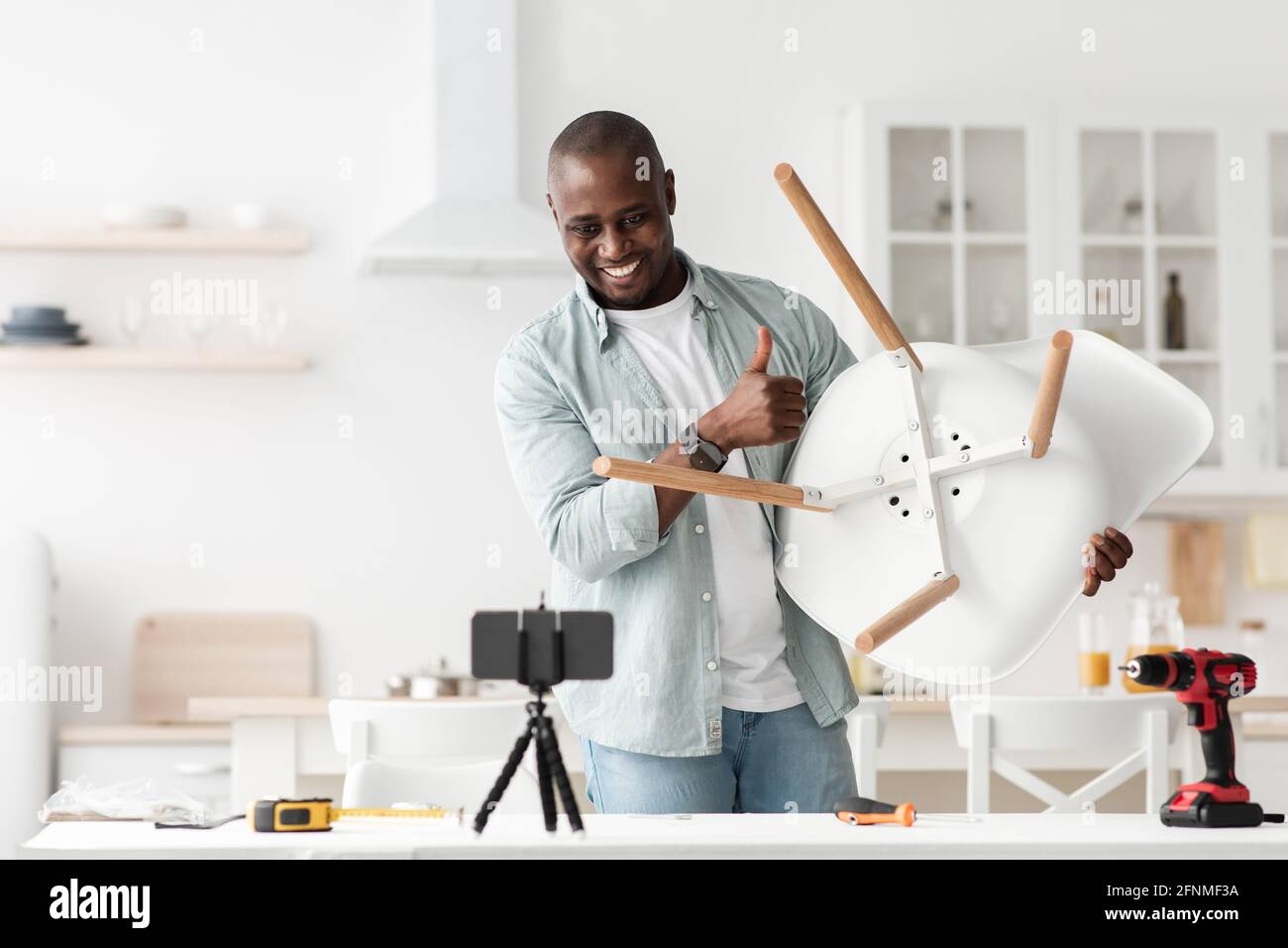 Blog about furniture repair and assembly. Happy african american man showing finished chair to smartphone camera Stock Photo