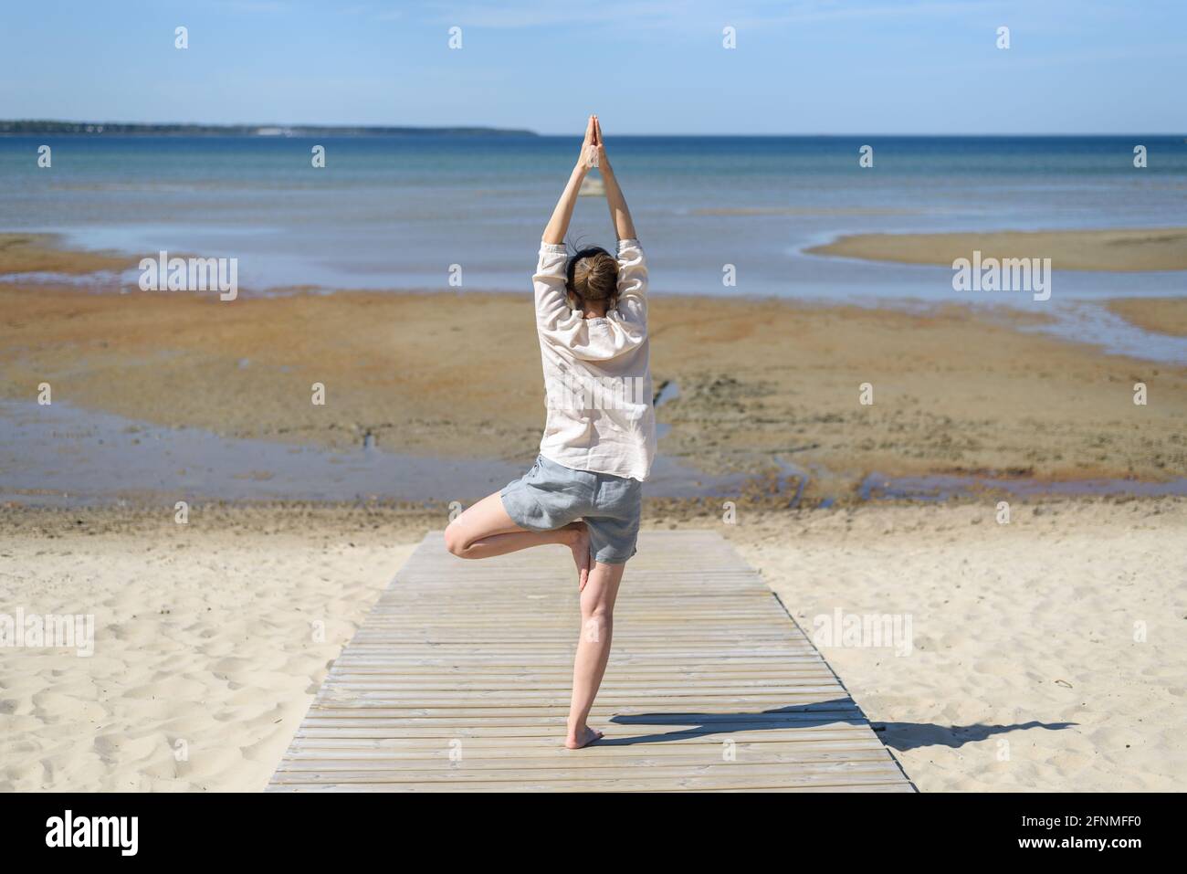 Woman in linen clothes doing yoga tree pose on beach at sunny day ...