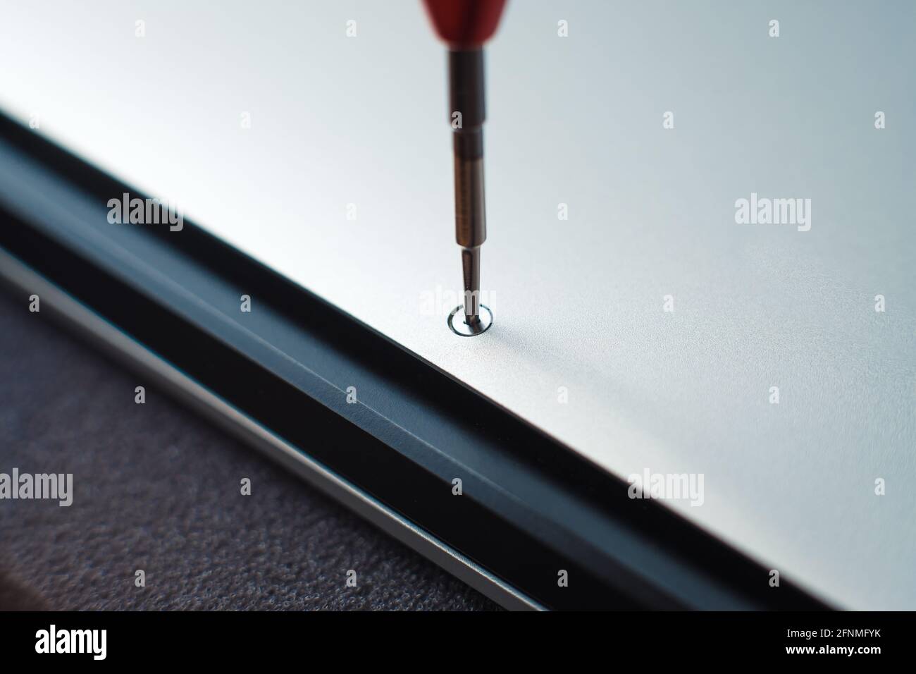 Master unscrewing small screw with magnetic screwdriver tool of broken laptop. Stock Photo