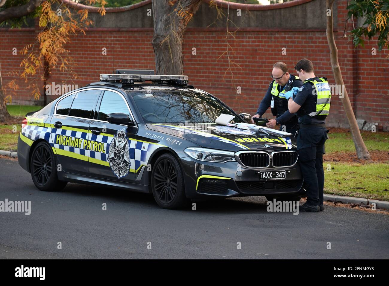 A Victoria Police Highway Patrol BMW M5 parked on the side of the road, while two police officers perform their duty Stock Photo