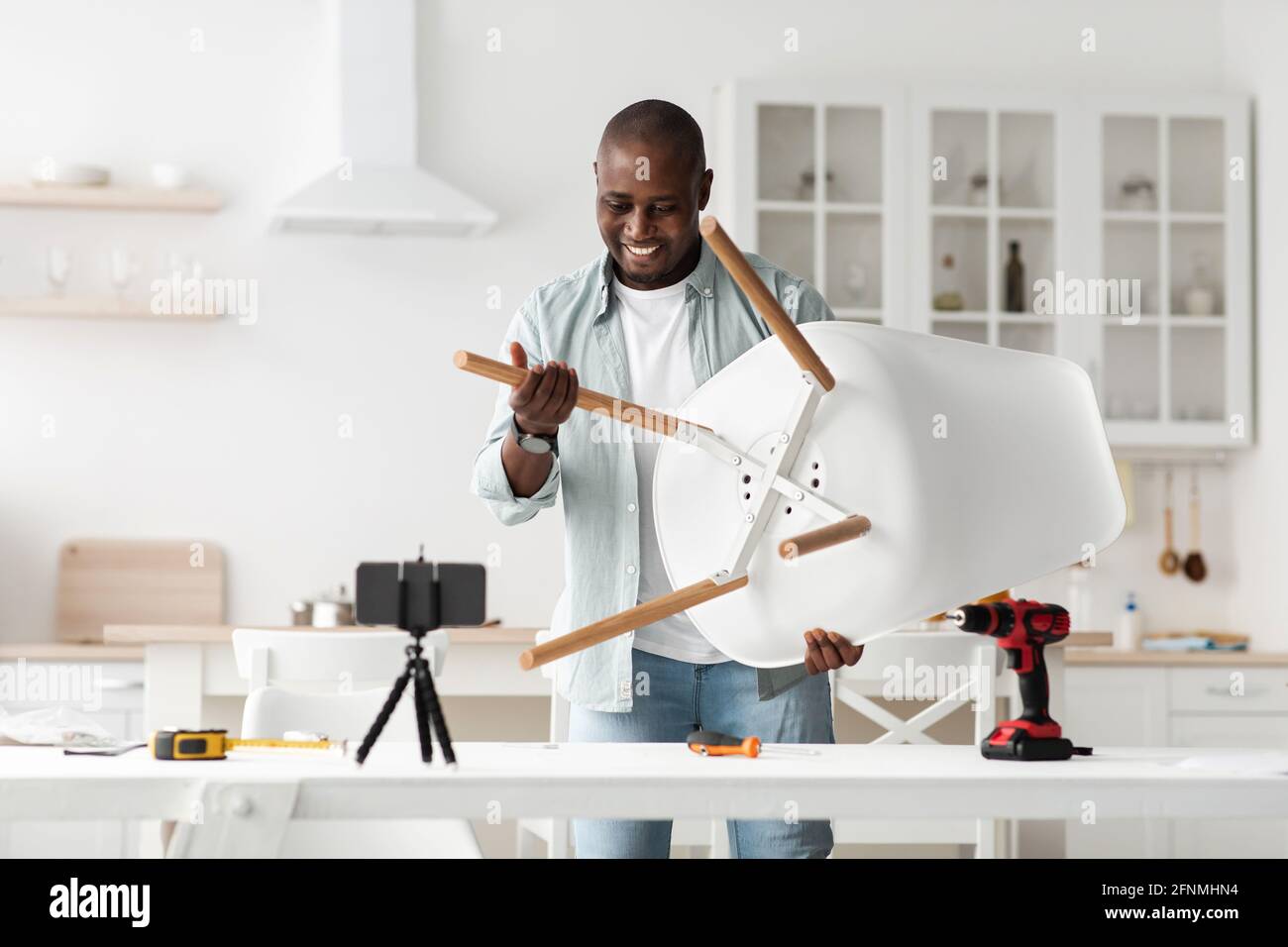 Remote work and blog about carpentry. Excited black handyman looking at smartphone webcam and showing finished chair Stock Photo