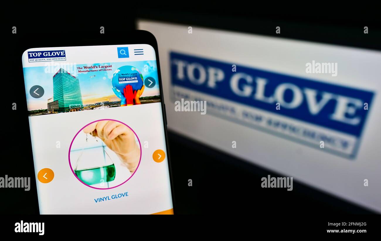 Cellphone with business webpage of Malaysian company Top Glove Corporation Berhad on screen in front of logo. Focus on center of phone display. Stock Photo