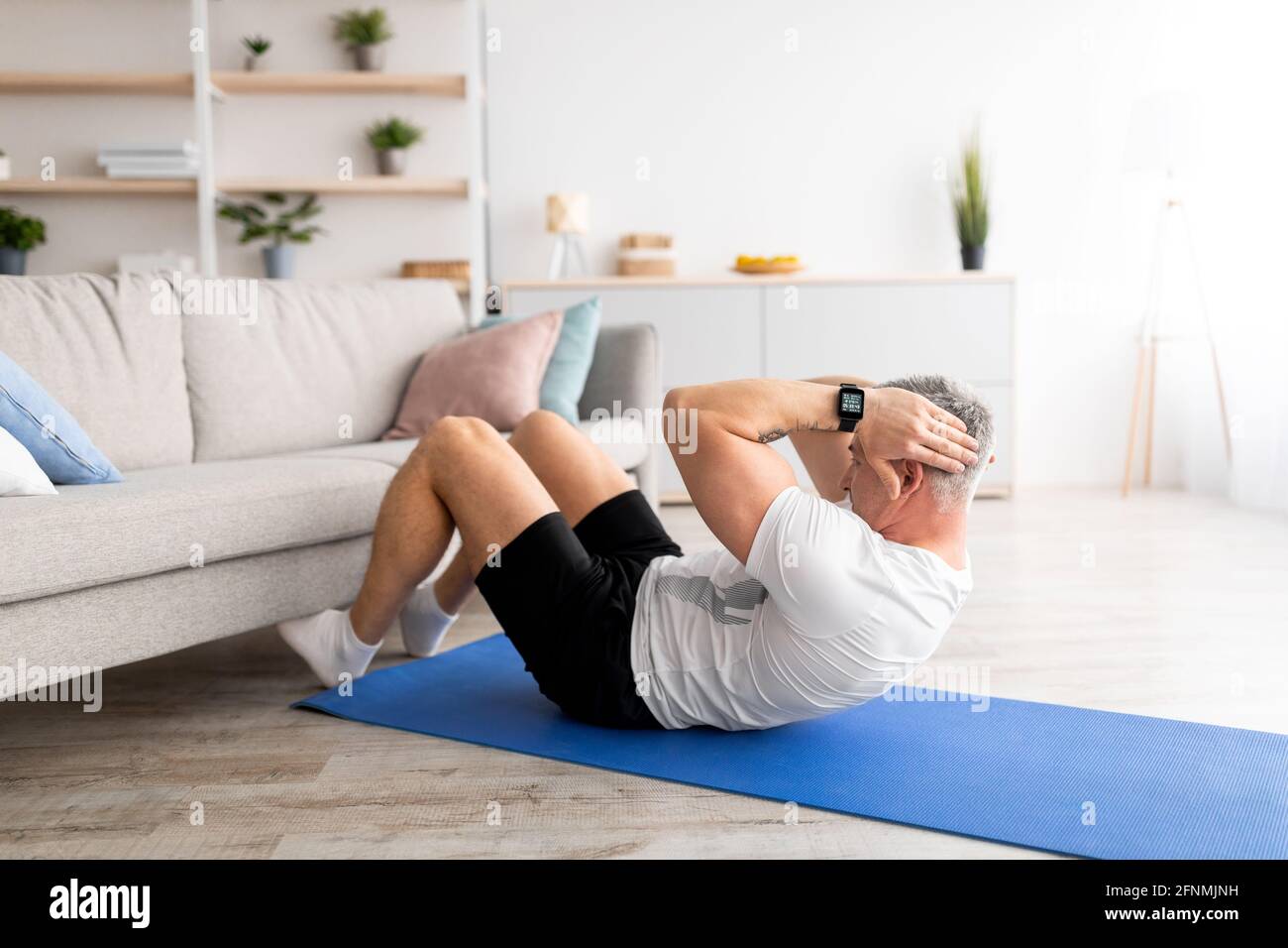 Workout at home. Mature man doing abs crunches near sofa, exercising in  living room at home Stock Photo - Alamy
