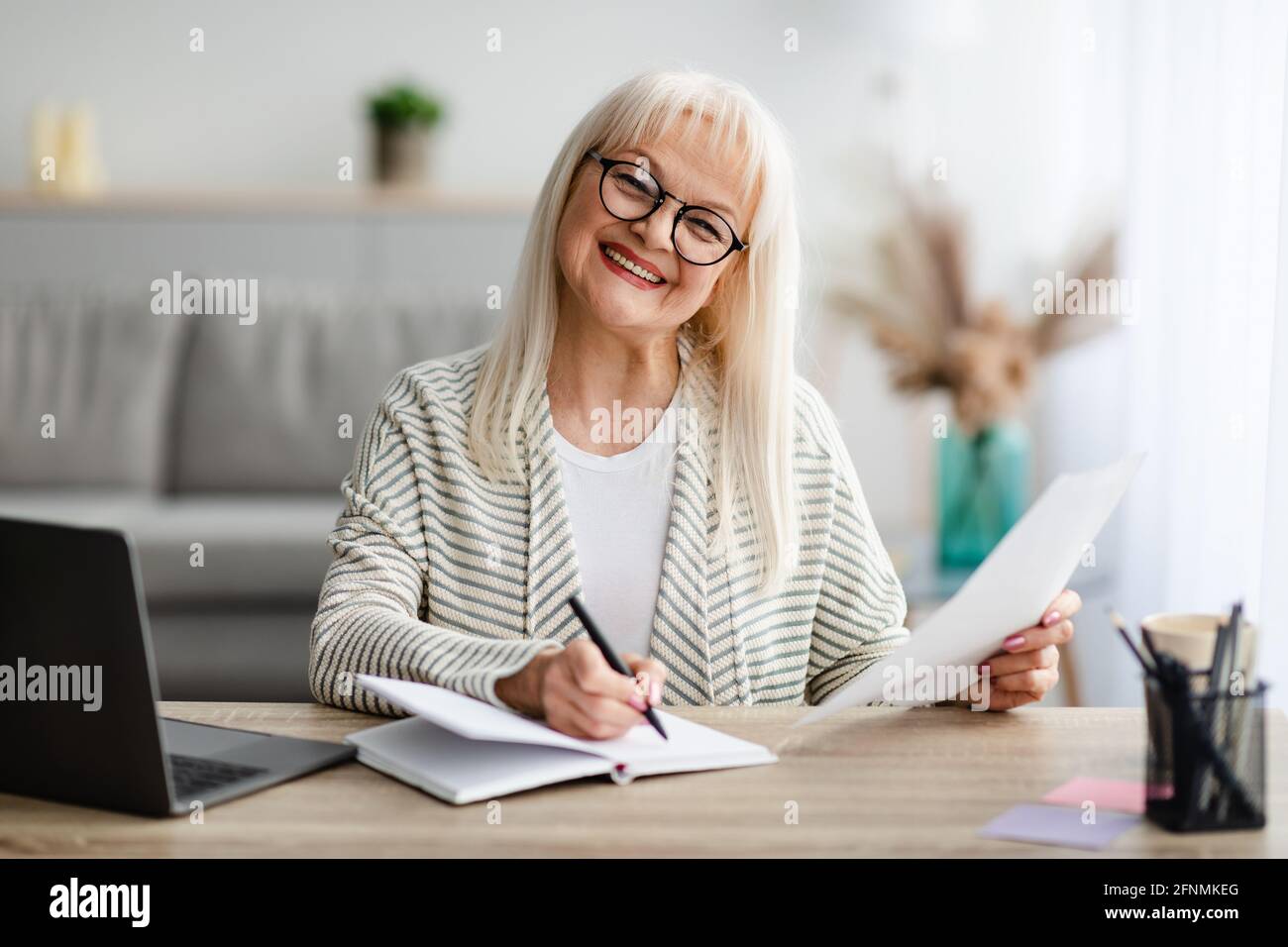 Smiling mature woman writing and holding document at home Stock Photo