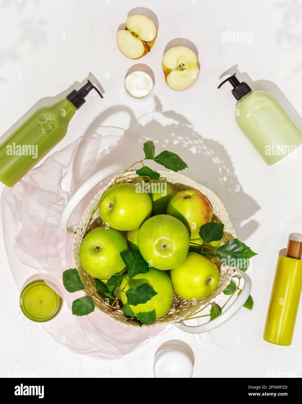 Vertical cosmetic composition with green apples, plastic bottles with cream, lotion, gel, scrub, soap on a white background. Summer beauty products Stock Photo