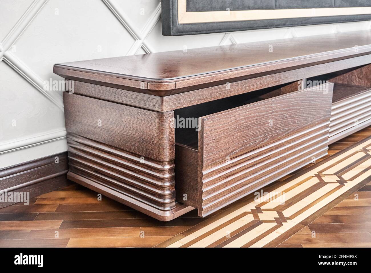 Elegant commode for TV set made of veneer and solid oak lumber toned in dark brown color on wood block parquet floor closeup Stock Photo