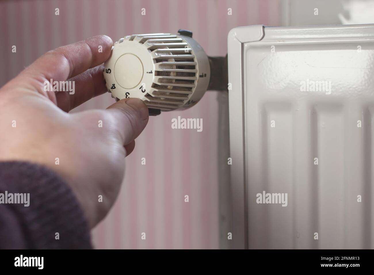 Hand turns off the radiator thermostat to a minimum with the arrival of