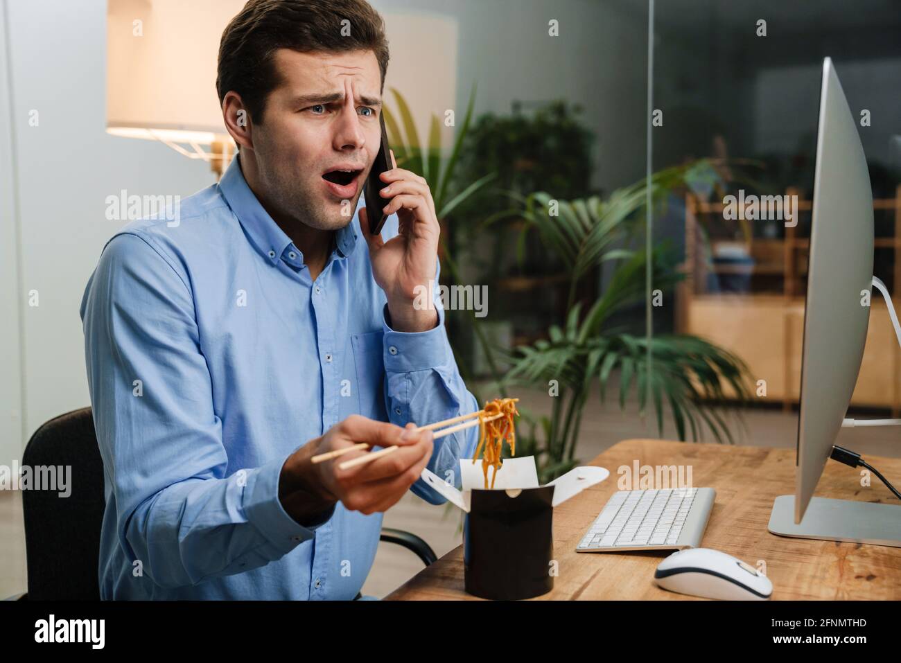 Confused handsome young business man using mobile phone while having lunch at the work Stock Photo