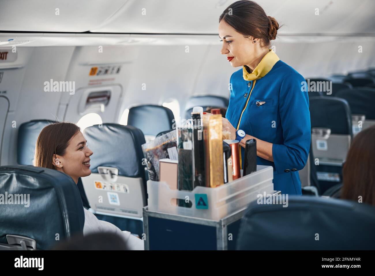 Woman on plane addressing flight attendant with food trolley Stock Photo Alamy