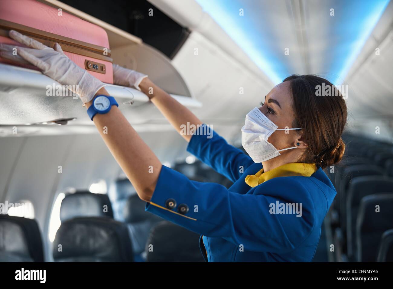 Cabin crew member shoving suitcase to overhead bin Stock Photo Alamy