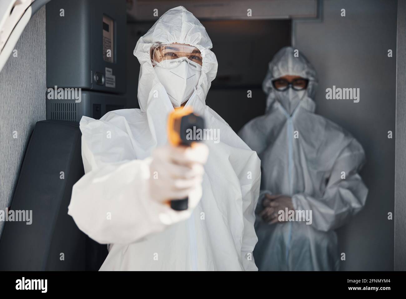 Female wearing disposable protective coverall holding laser thermometer Stock Photo