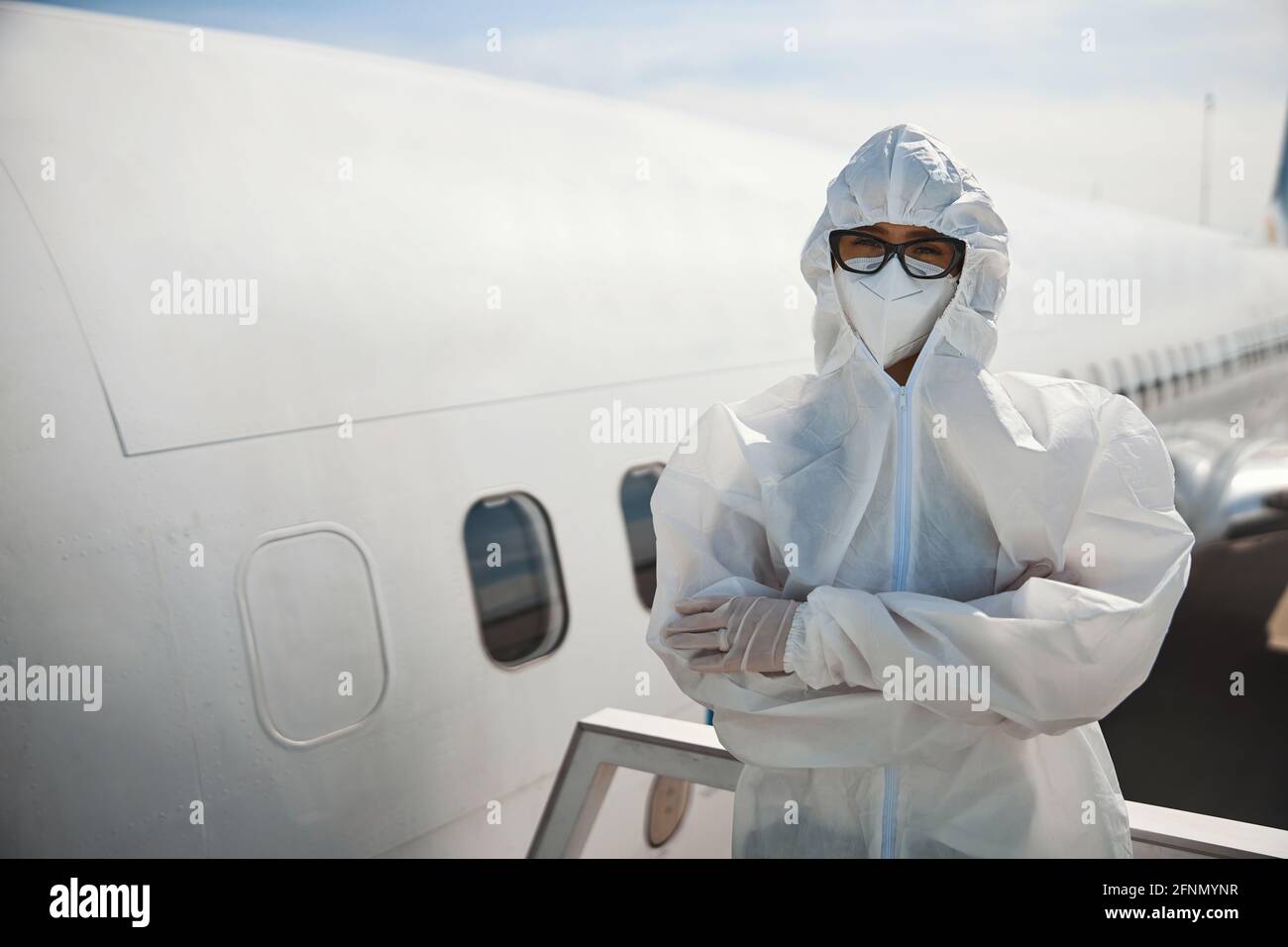 One woman in hooded protective clothes crossing arms near airplane Stock Photo