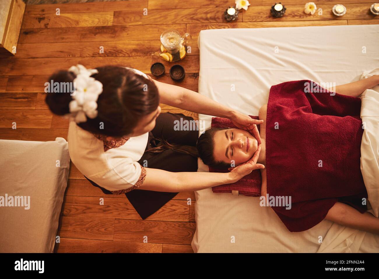 Massage specialist placing her hands below lying woman chin Stock Photo