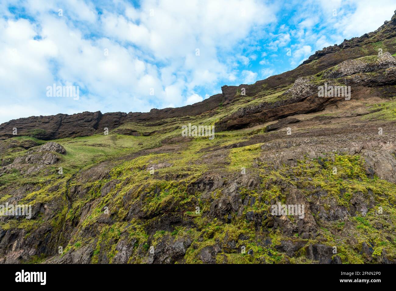Low angle view of a steep grassy cliff under blue sky with clouds. Natural background. Stock Photo