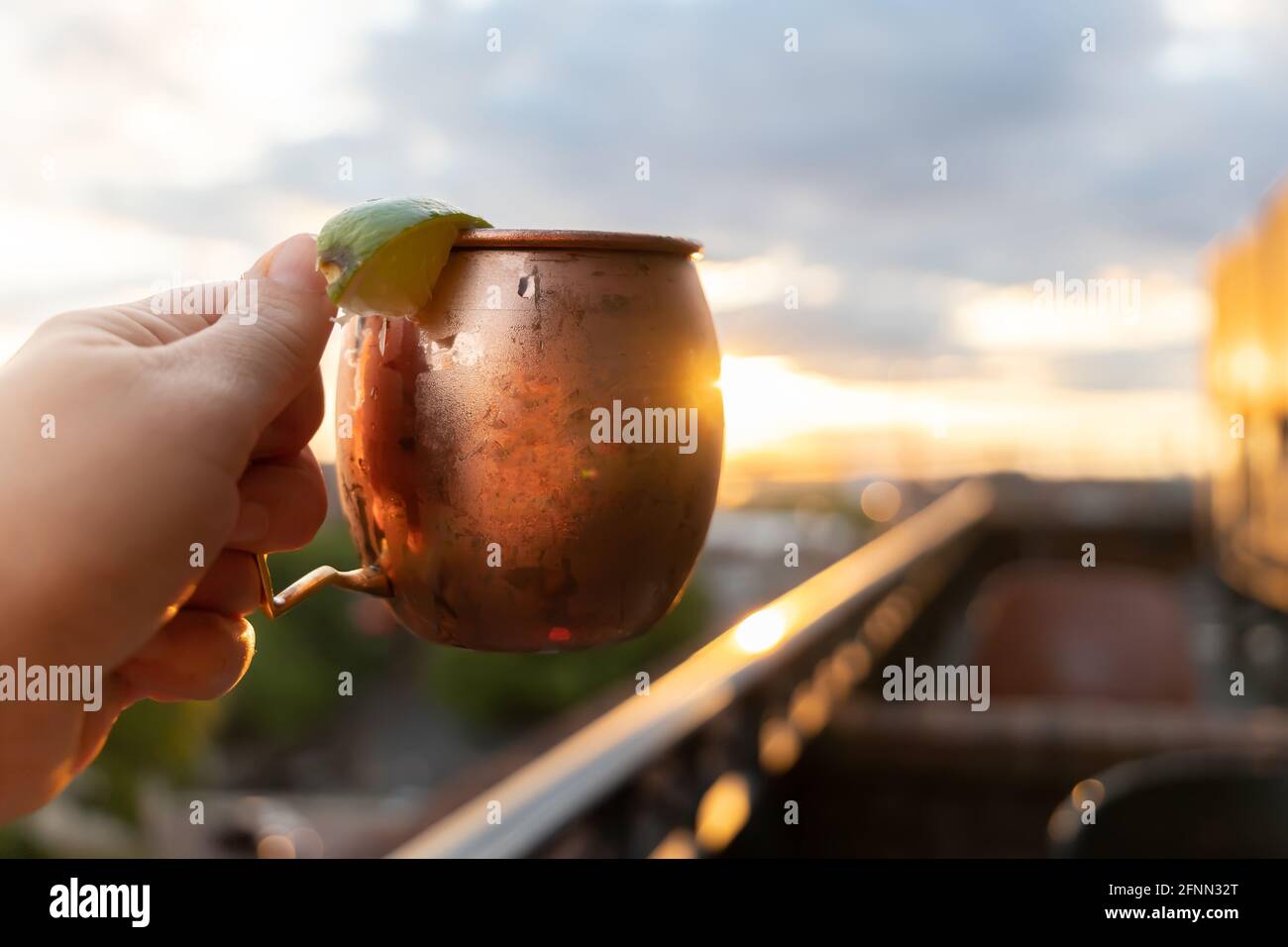 A moscow mule held up at a rooftop restaurant bar at sunset Stock Photo