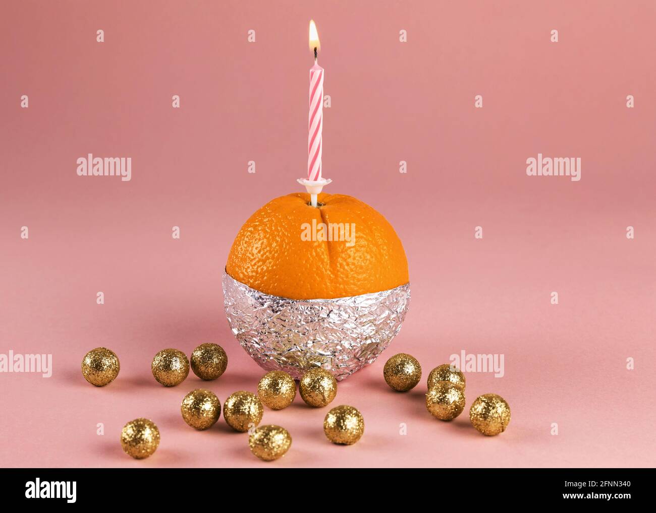 Fresh orange in aluminium foil with a lighted candle and with golden