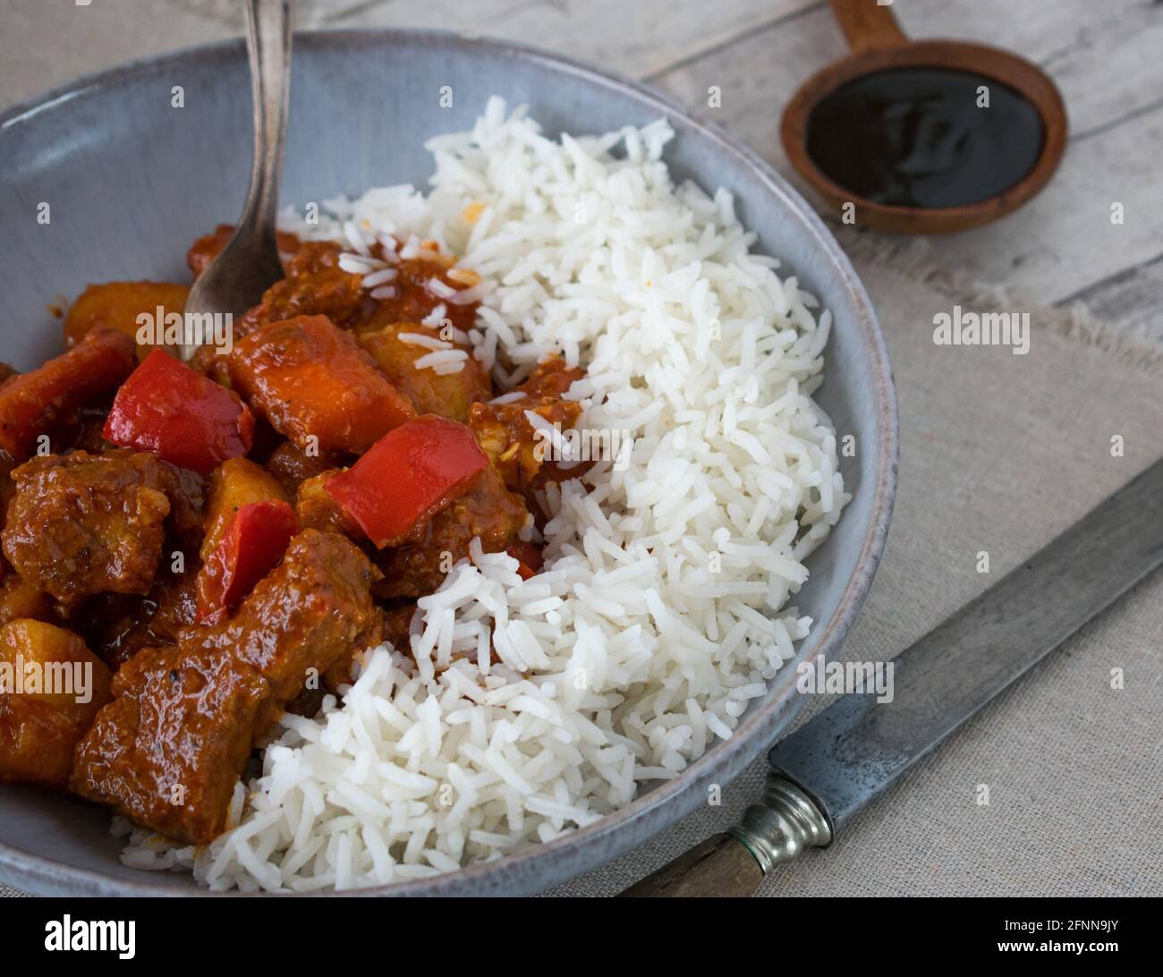 Spicy filipino pork stew afritada served with basmati rice in a rustic bowl on wooden table Stock Photo