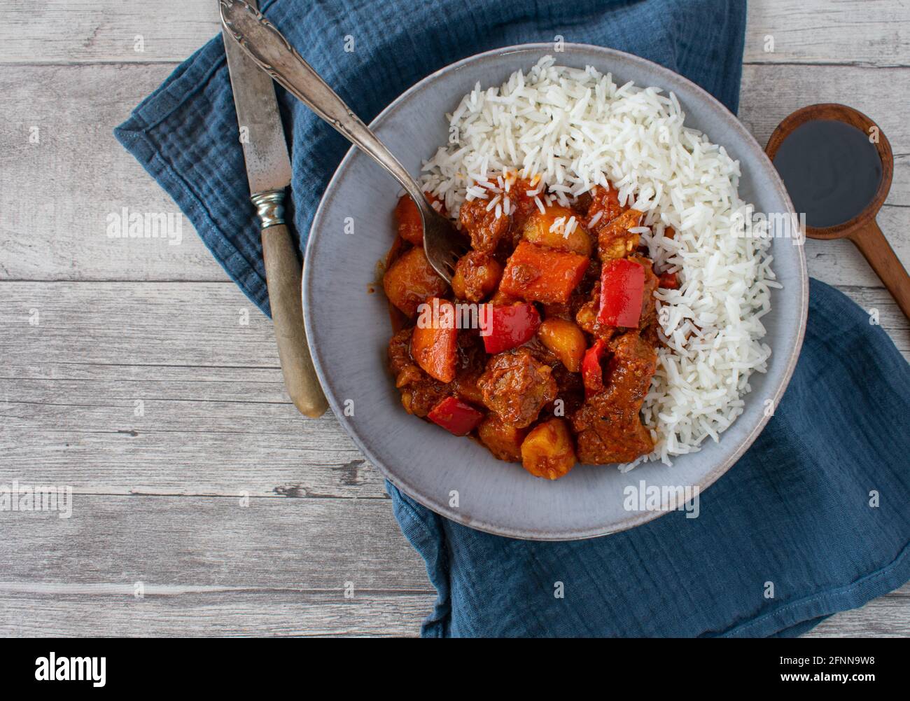 Spicy pork stew afritada served with basmati rice in a rustic bowl on wooden table background Stock Photo
