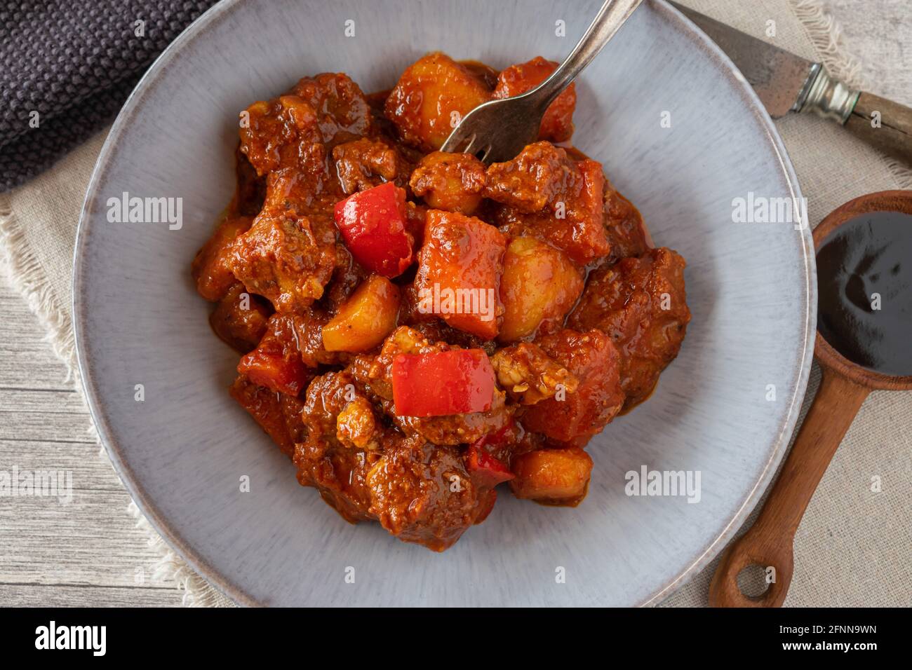 filipino pork stew afritada served on plate with fork on rustic table with fish sauce Stock Photo