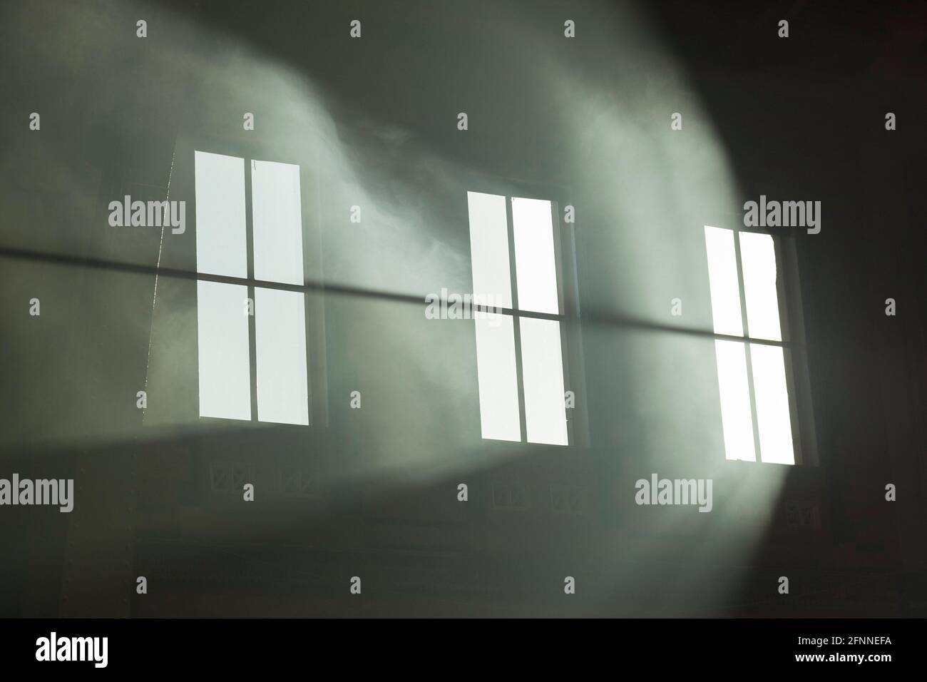 Atmospheric sunbeams streaming through the the windows of a large old building. The dusty interior atmosphere has created these striking beams Stock Photo