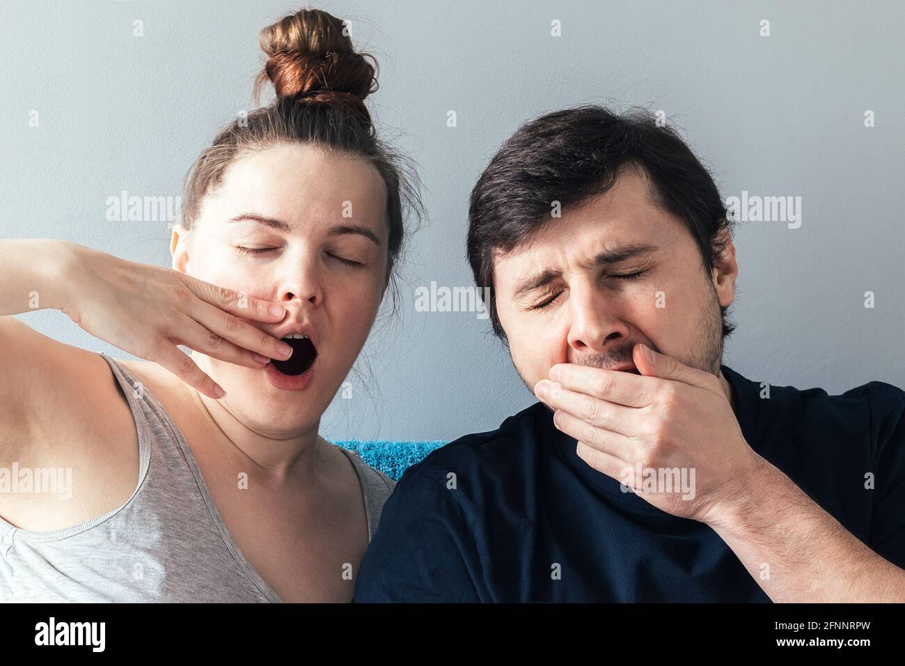 Yawning Caucasian couple with eyes closed. Man and woman, yawning and covering wide open mouth with hand. Tired and sleepy expression Stock Photo