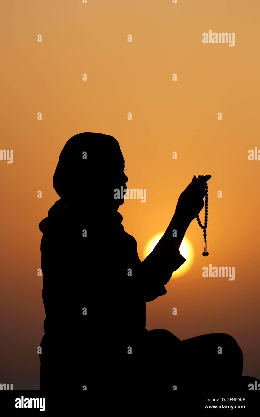 Silhouette of muslim woman holding prayer beads in   her hands and praying at sunset. Religion praying concept.  United Arab Emirates Stock Photo