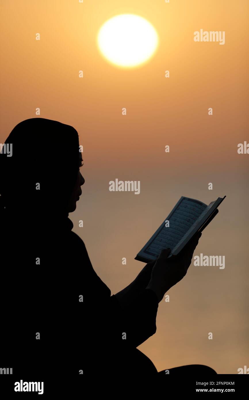 Silhouette of muslim woman reading the Noble Quran   at sunset. Religion praying concept. United Arab Emirates Stock Photo