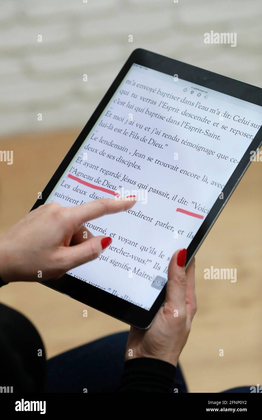 Woman reading and studying the gospels of the bible  on a  digital tablet Ipad.  France. Stock Photo