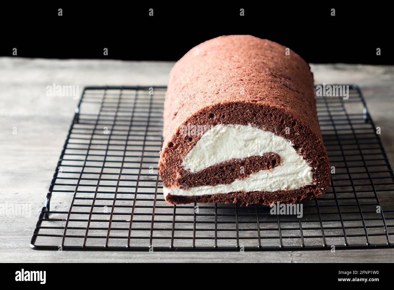 A fresh home made gluten free chocolate Swiss Roll, filled with a mascarpone whipped cream filling has been rolled and sits on a cooling rack Stock Photo