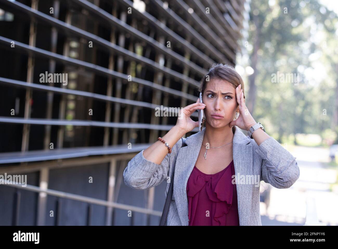 Stressed young business woman talking on mobile phone in front of office building Stock Photo