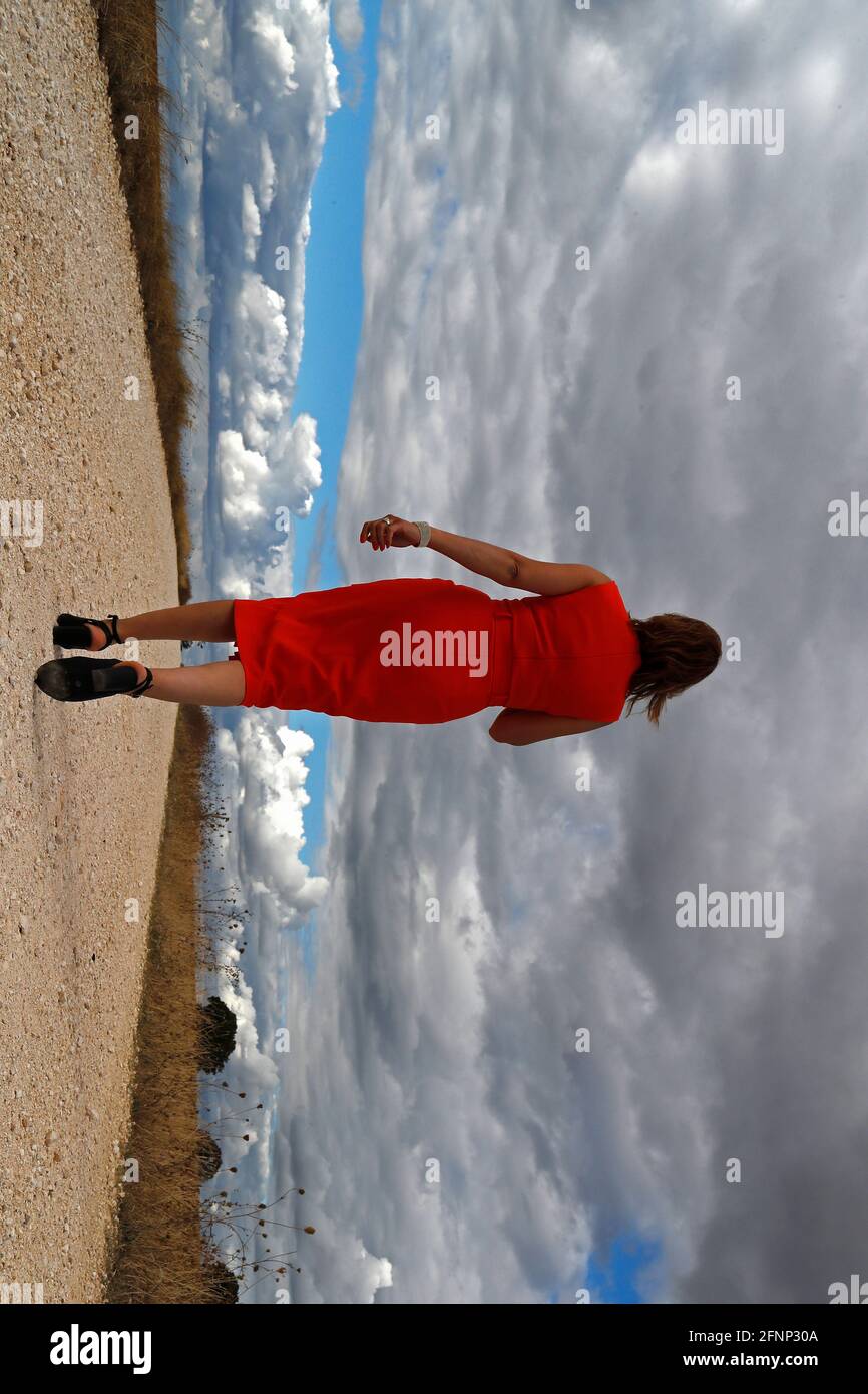Back view of a woman walking alone away on straight country road. Cloudy sky. France. Stock Photo