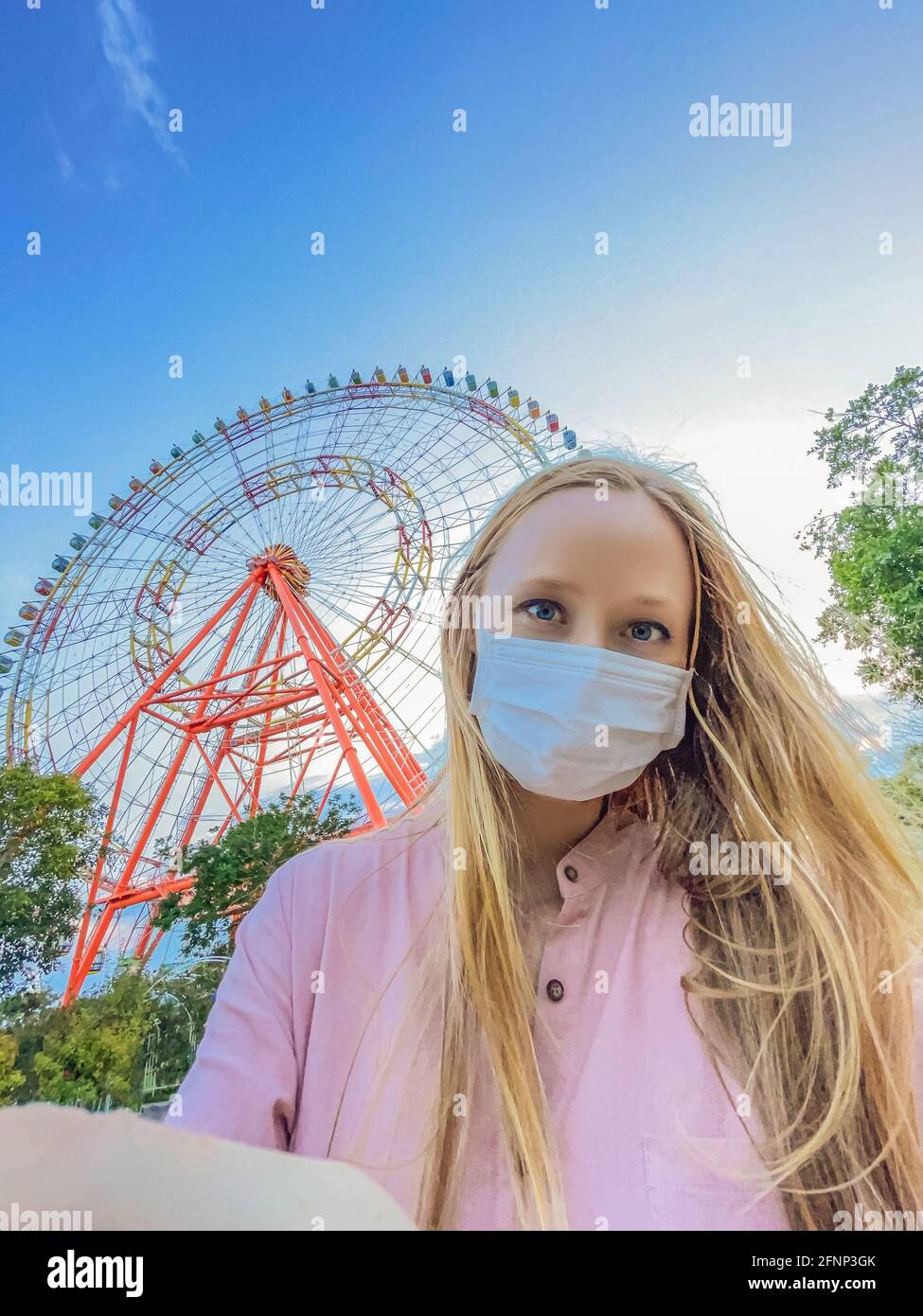 A woman in a pink dress takes a selfie on the background of a ferris wheel Stock Photo
